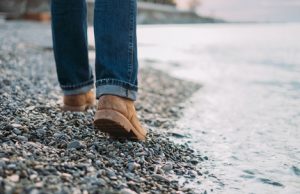 Unrecognizable man walking on pebble coast near the sea, view of legs. Rear view